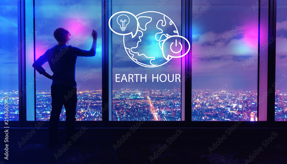 Earth hour with man writing on large windows high above a sprawling city at night