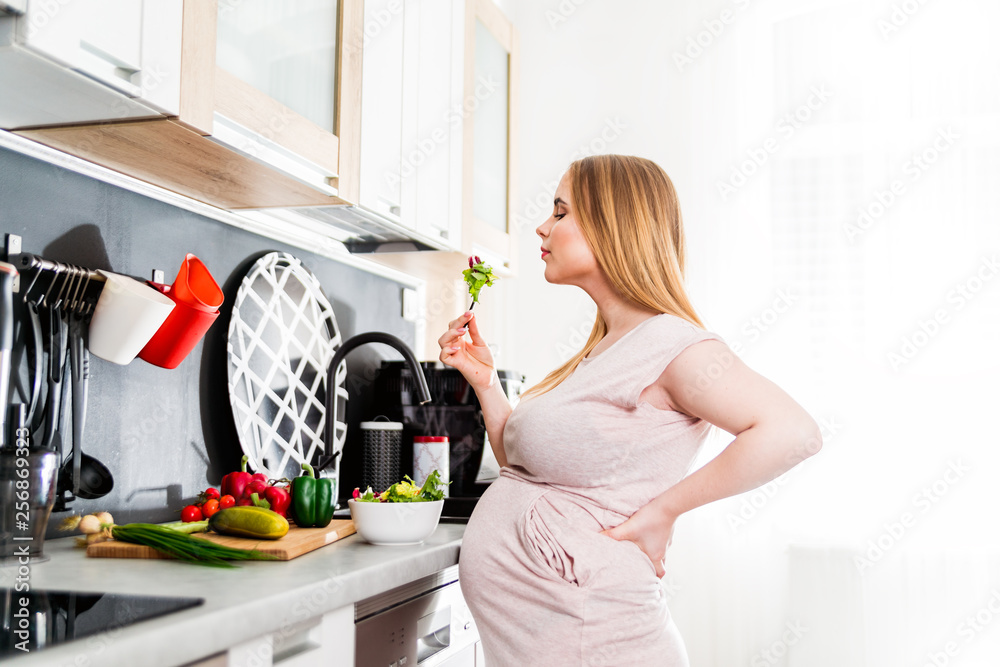 Happy pregnant woman eating vegetable salad in kitchen, health during pregnancy concept