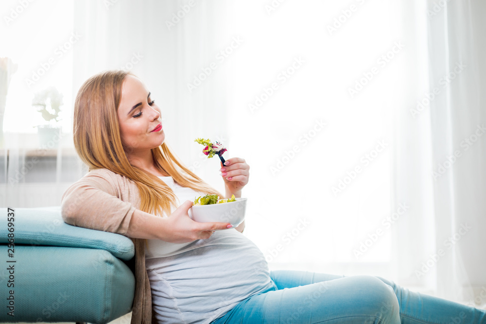 Happy pregnant woman at home eating vegetable salad at home