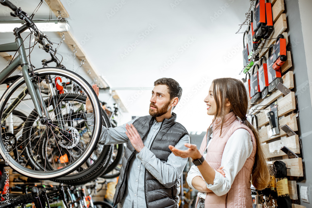 Salesman helping young woman to choose a new bicycle to buy standing in the bicycle shop