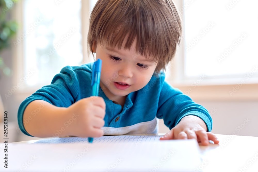 Toddler boy drawing with pen and paper at his desk