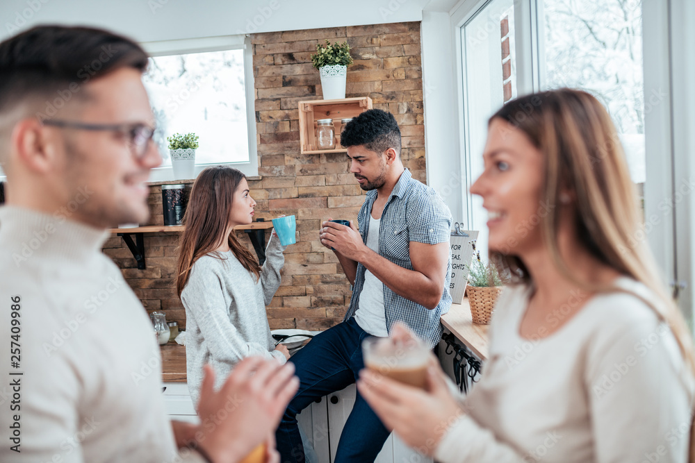 Two young couples talking in the kitchen on winter vacation morning, focus on the background.