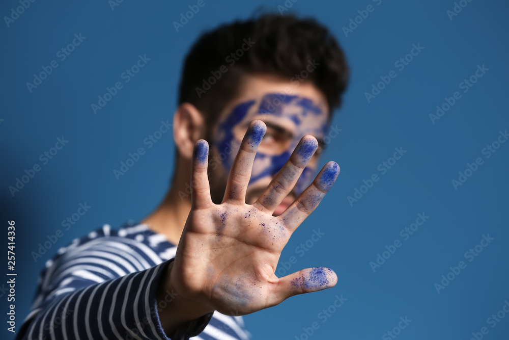 Handsome man with paint on his hand and face against color background