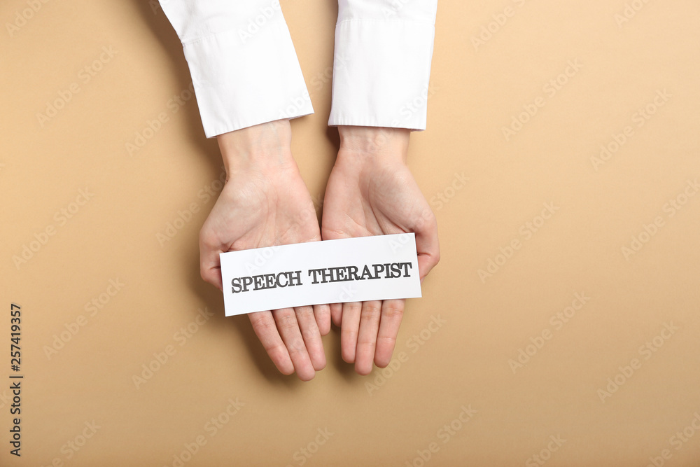 Doctor holding paper with text SPEECH THERAPIST on color background