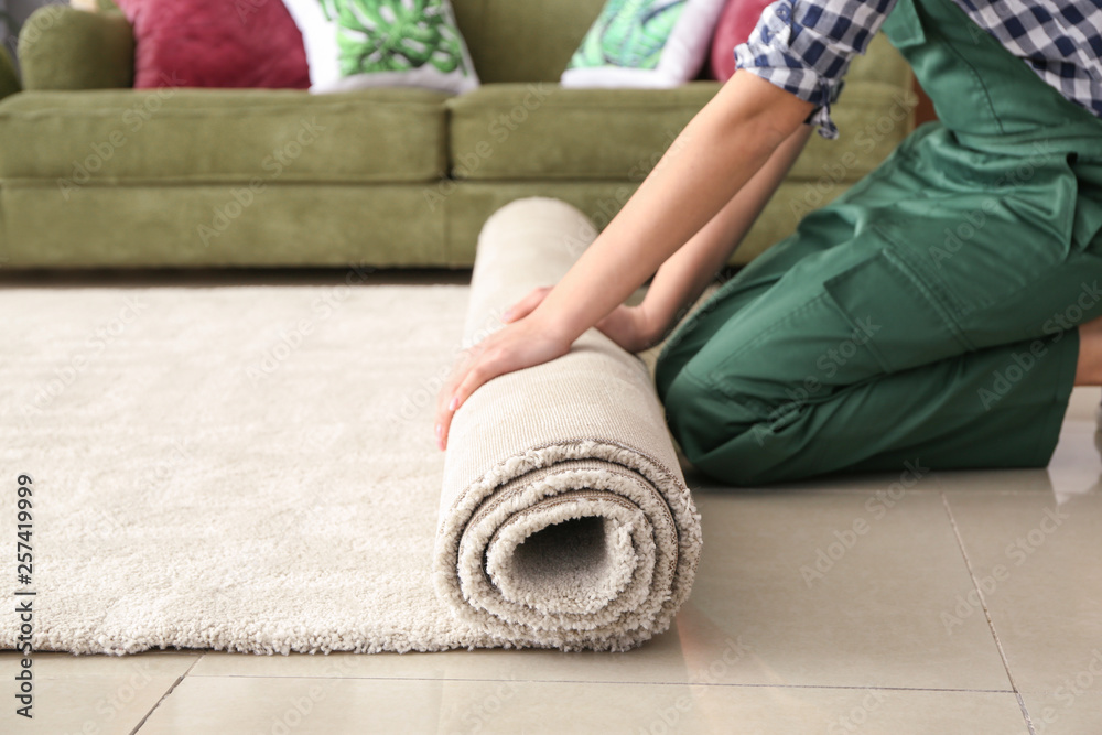 Worker rolling carpet on floor in room