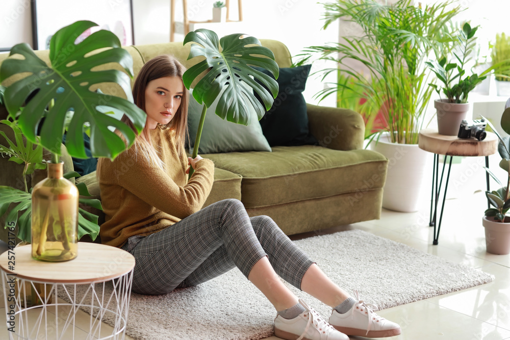 Portrait of beautiful woman with green tropical leaves indoors