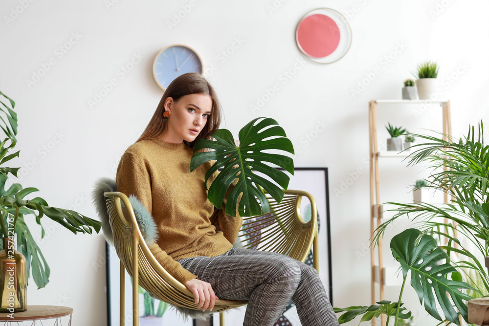 Portrait of beautiful woman with green tropical leaves indoors