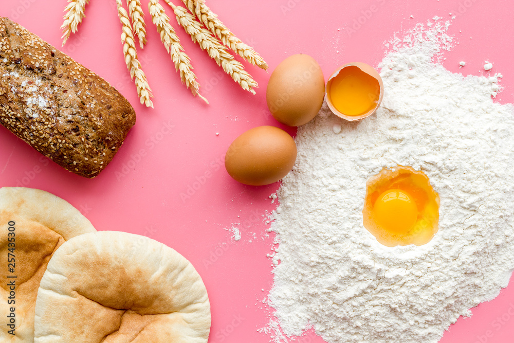 Ingredients for homemade bread. Bread near wheat ears, flour and eggs on pink background top view