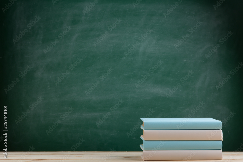 Education and reading concept - group of colorful books on the wooden table in the classroom, blackb