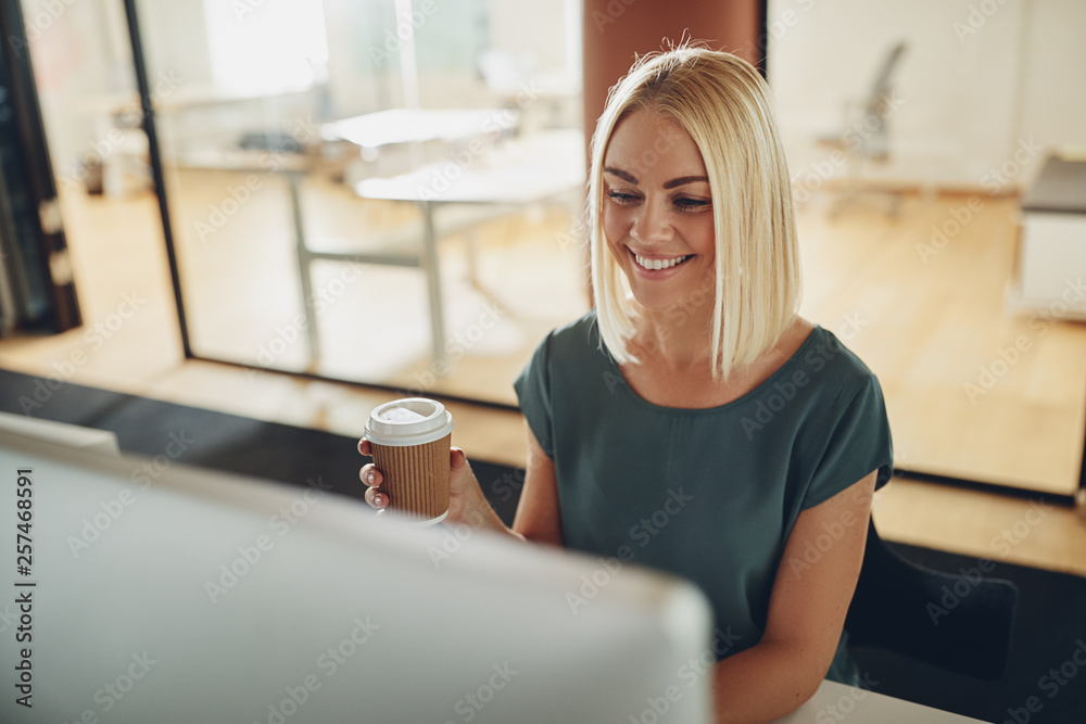 Smiling businesswoman enjoying a coffee while working in an offi