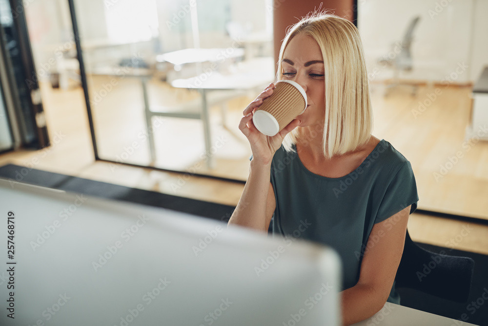 年轻的女商人坐在办公桌前喝咖啡