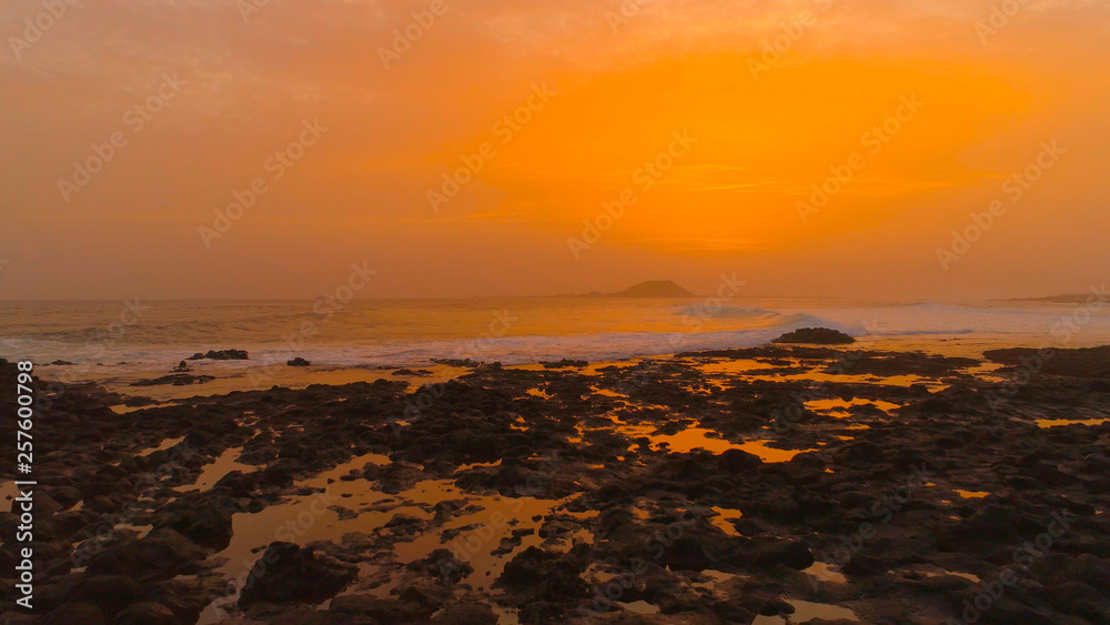 Foaming water coming from the ocean cleansing the rocky black beach at sunset.