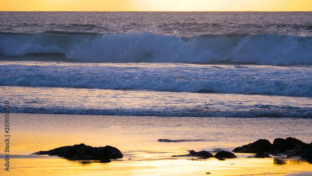 Small waves crash and wash the empty sandy shore of tropical island at sunset.