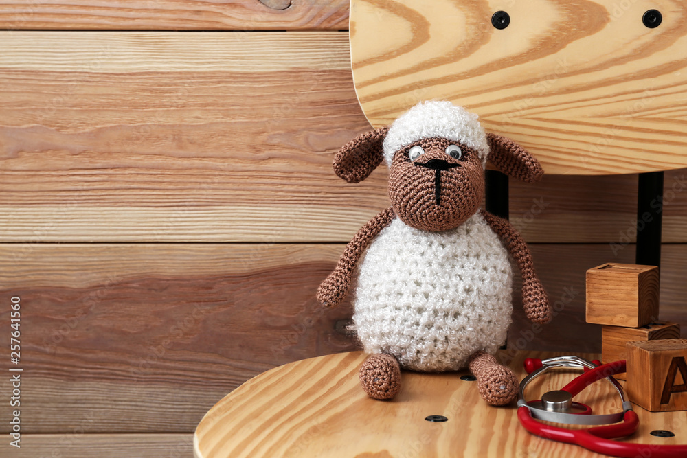 Cute sheep toy with stethoscope on wooden chair. Health care for kids