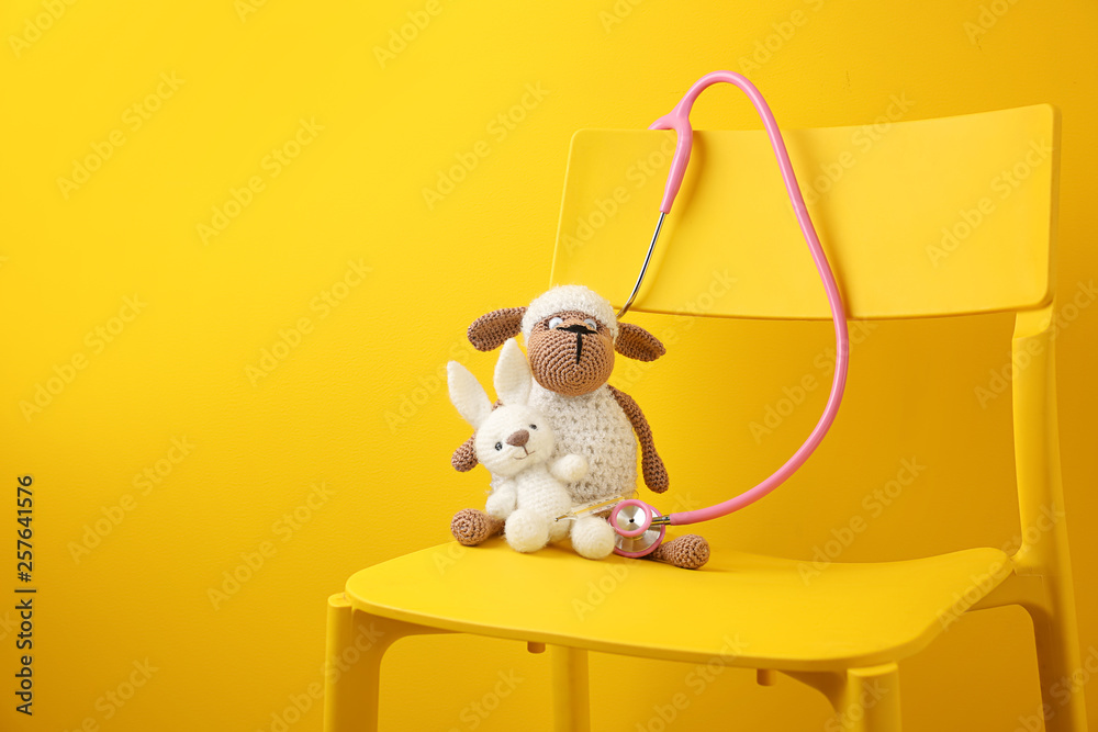 Cute toys with stethoscope on chair against color background. Health care for kids