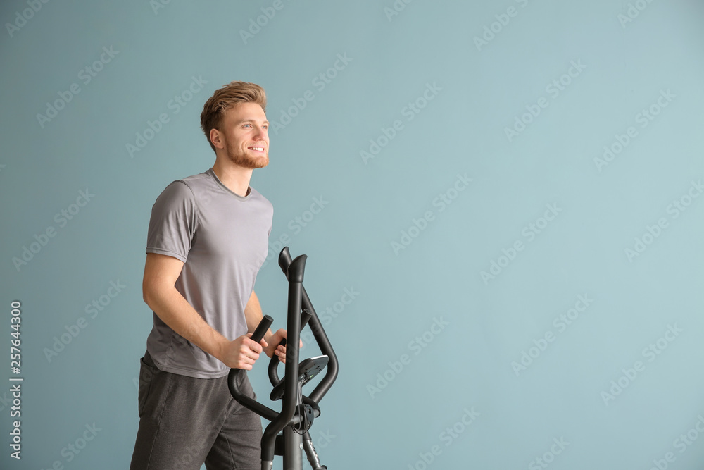 Sporty young man training on machine against color background