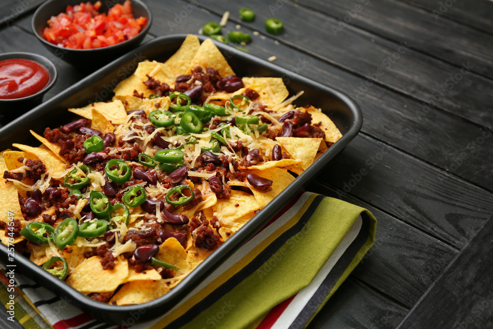 Baking dish with tasty nachos, minced meat and chili on wooden table