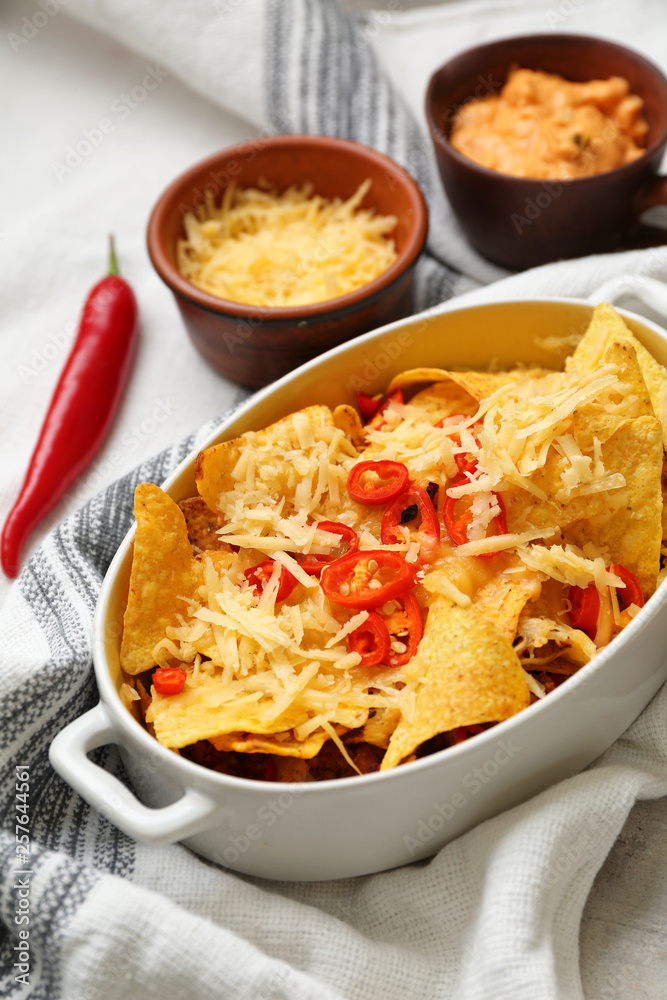 Baking dish with tasty nachos, cheese and chili on table