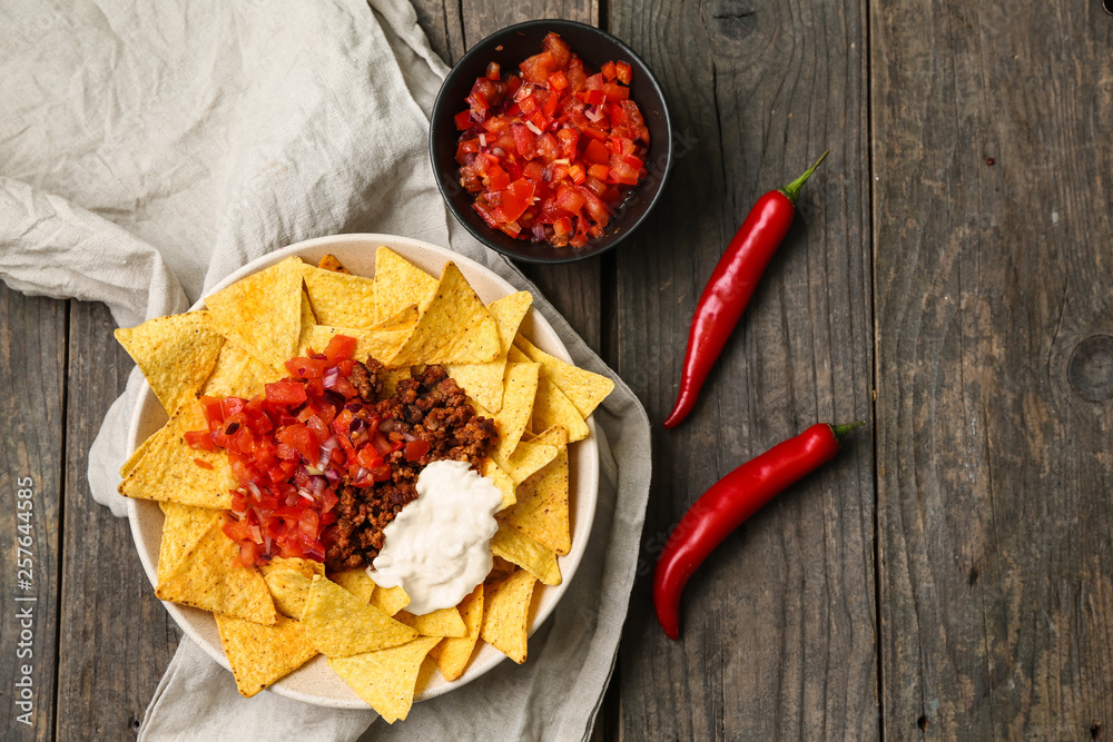 Plate with tasty nachos, minced meat and salsa on wooden table