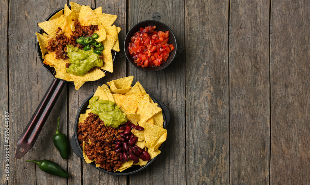 Frying pans with tasty nachos, minced meat, beans and guacamole on wooden table