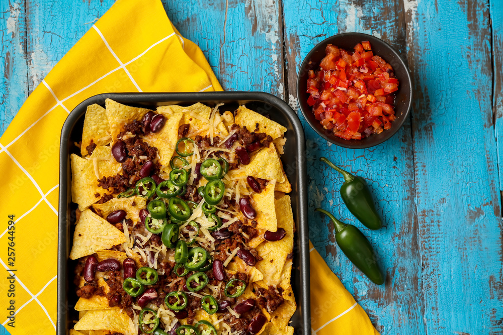 Baking dish with tasty nachos, minced meat and chili on wooden table