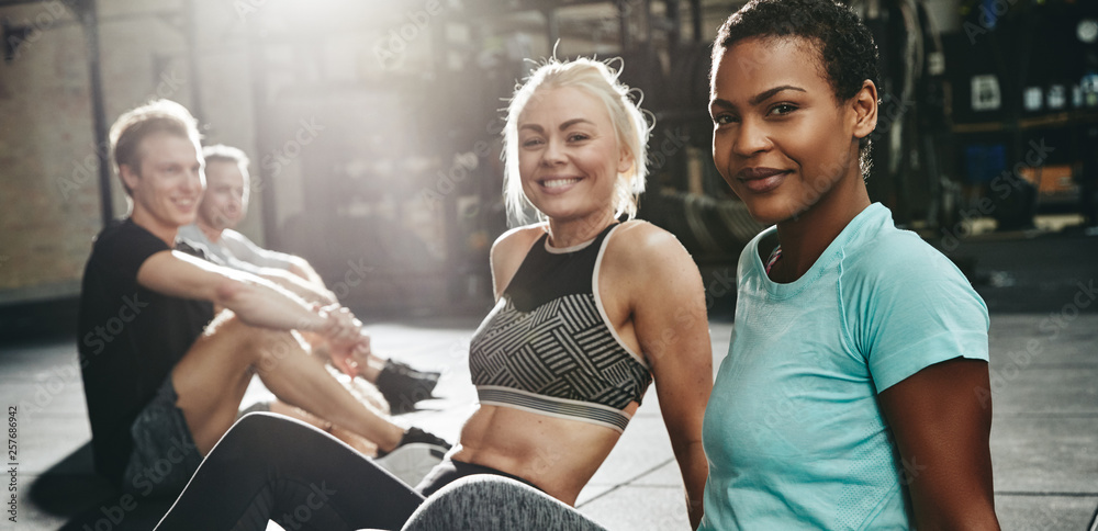 Two smiling young women sitting together on a gym floor