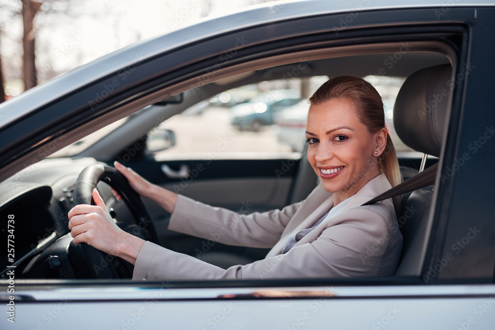 Portrait of a beautiful happy woman driving a car, smiling at camera.