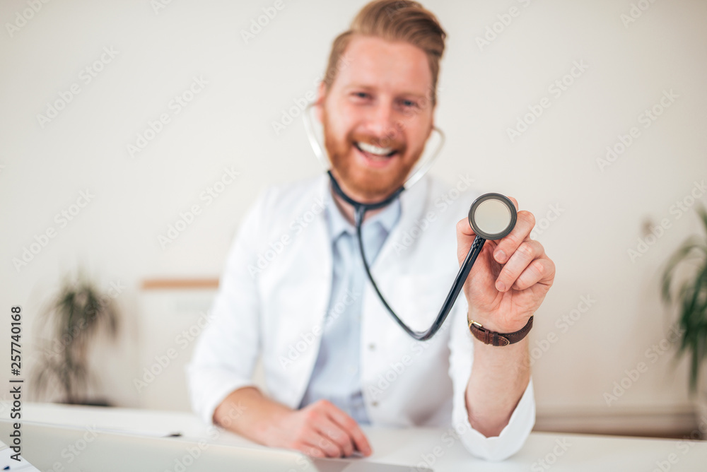 Portrait of a friendly handsome male doctor dressed in uniform holding stethoscope.