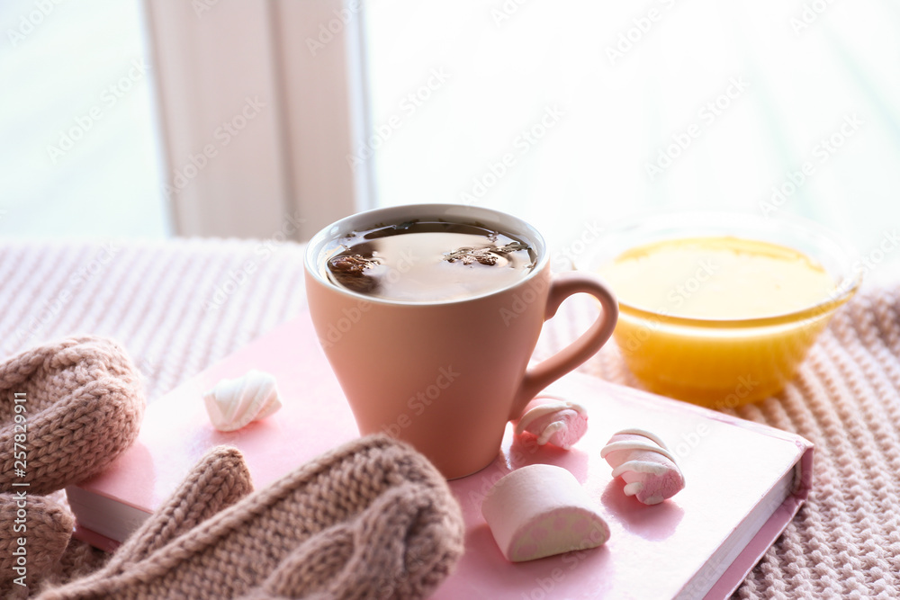 Cup of tea with honey, sweets and book on plaid near window