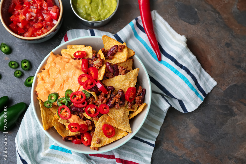 Plate with tasty nachos, minced meat and chili on grey table