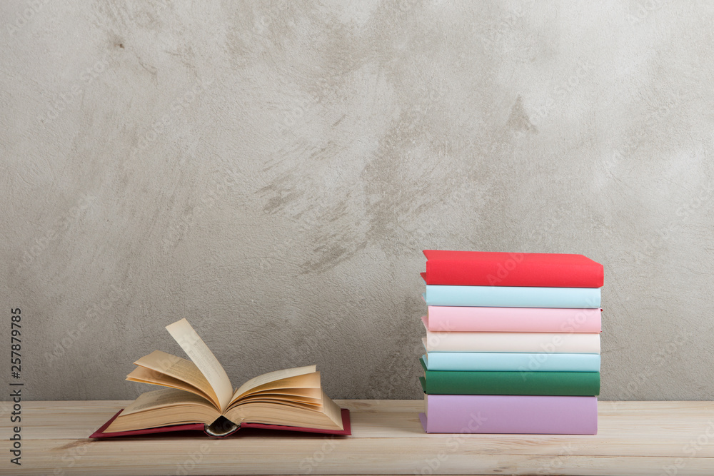 Education and reading concept - group of colorful books on the wooden table, concrete wall blackboar