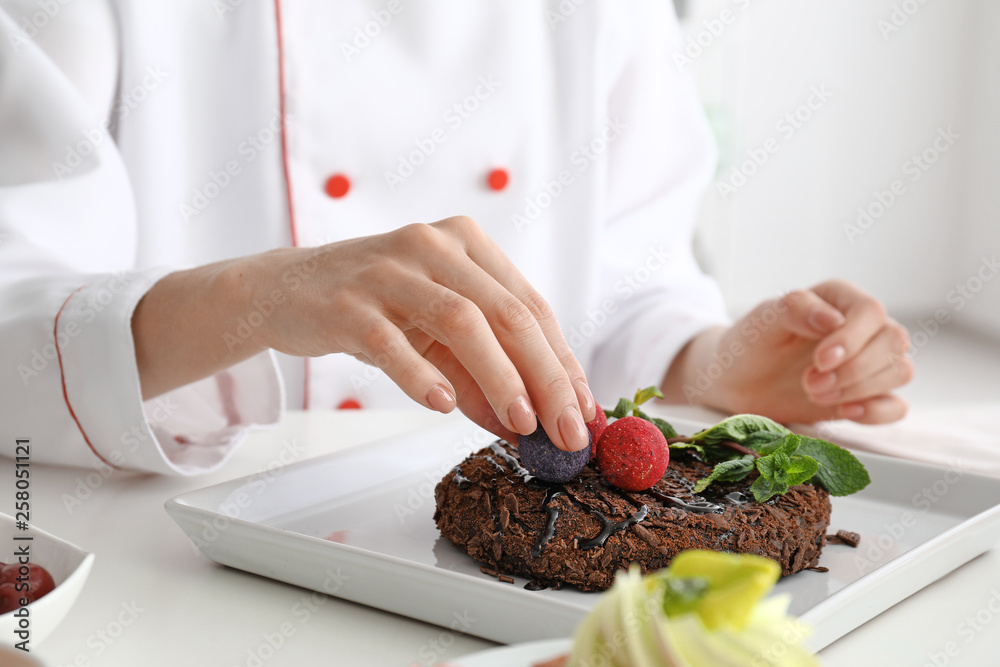 Young female confectioner decorating tasty dessert in kitchen