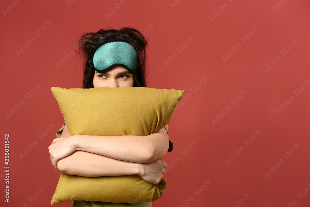 Sleepy young woman with mask and pillow on color background