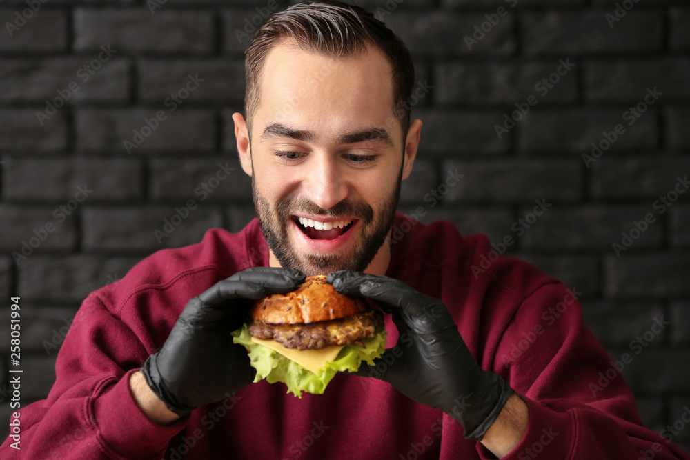 Man eating tasty burger on dark background