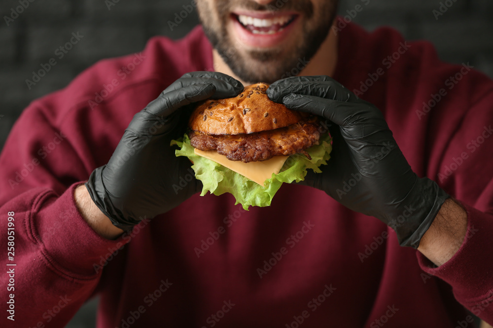 Man eating tasty burger on dark background, closeup