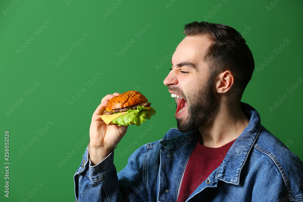 Man eating tasty burger on color background