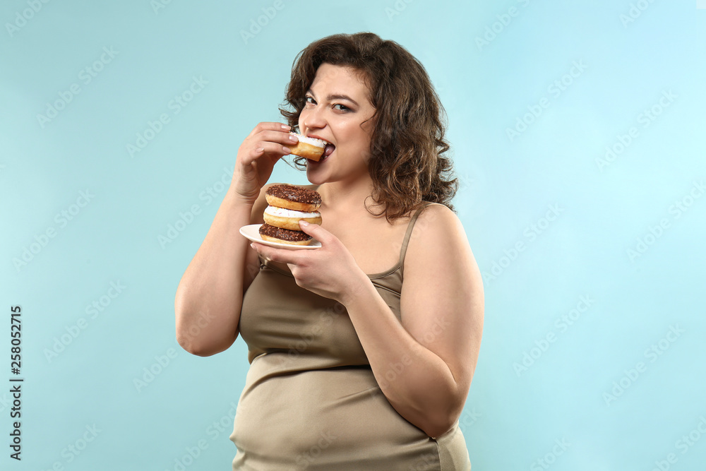 Overweight woman with donuts on color background