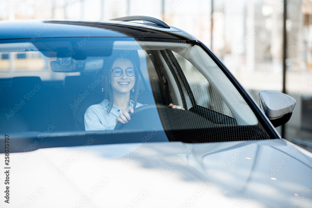 年轻快乐的女人在城市里开着豪车，挡风玻璃前视图