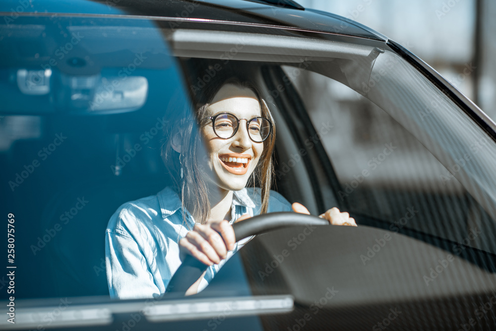 年轻快乐的女人开着豪车，阳光透过挡风玻璃的正视图