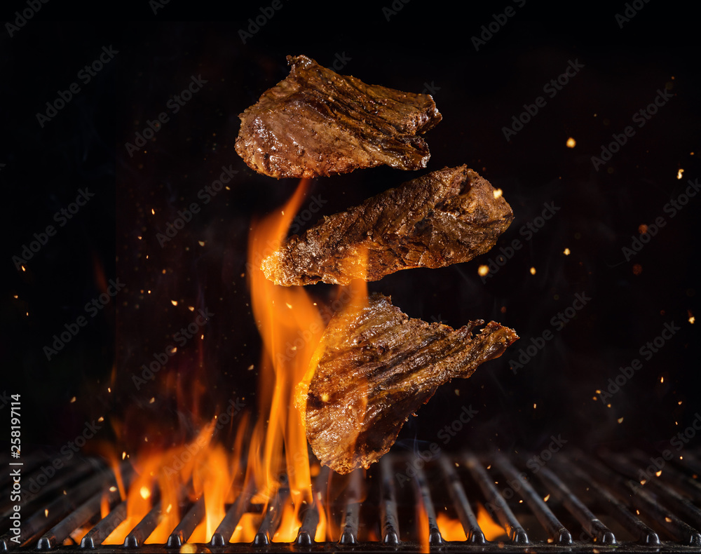 Flying beef steaks above burning grill grid