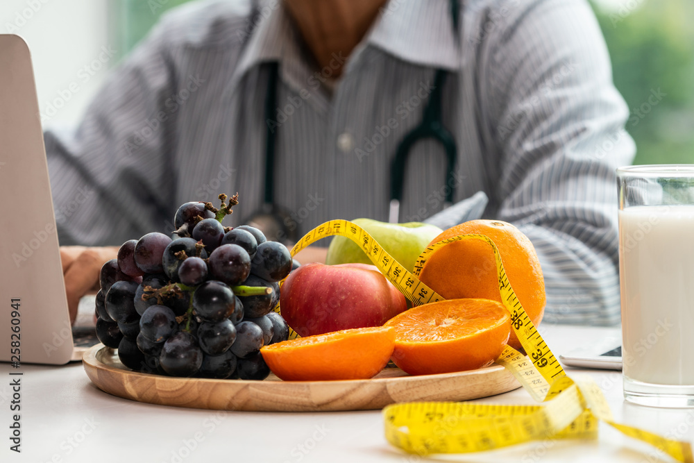 Senior male nutritionist doctor working on desk with healthy food fruits and milk on table in the ho