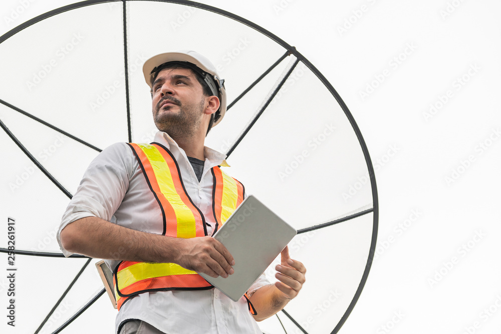 Professional technician or engineer standing on roof top of building working with satellite dish. Co