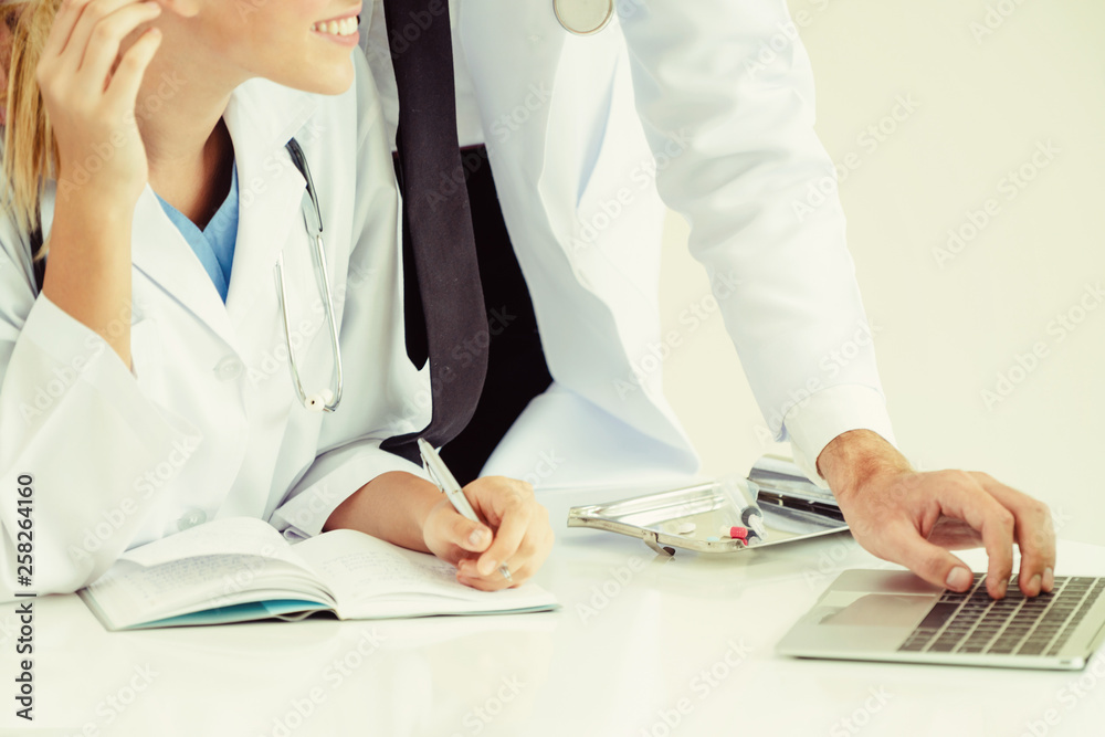 Doctor at hospital office working on laptop computer on the table with another doctor having discuss