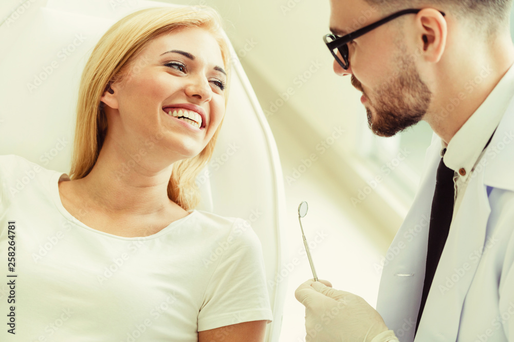 Young handsome dentist talks with happy woman patient sitting on dentist chair in dental clinic. Den