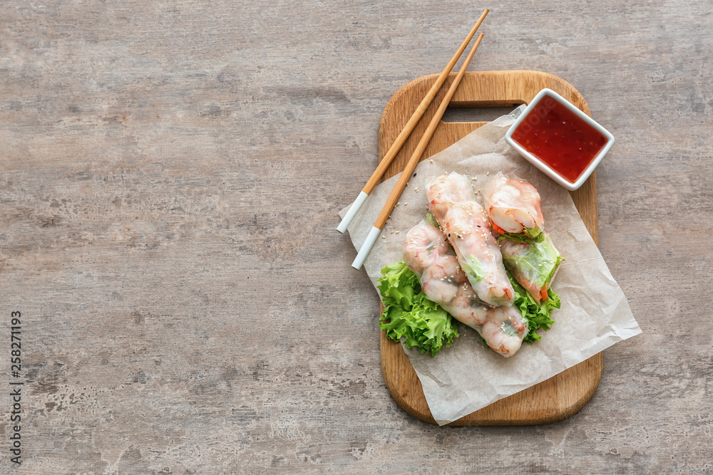 Board with tasty spring rolls and sauce on table