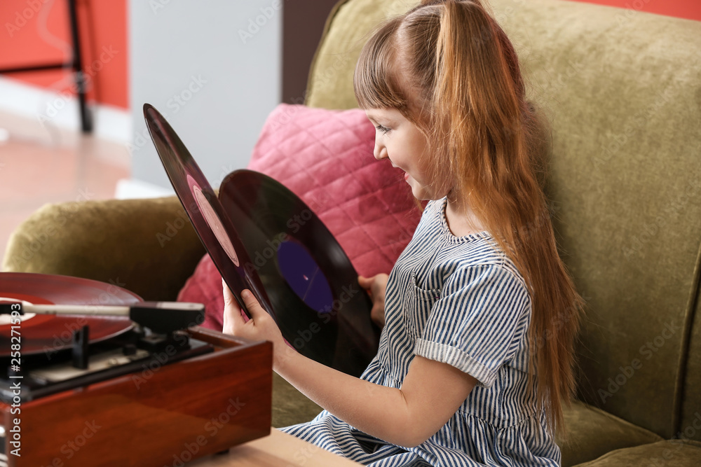 Cute little girl listening to music through record player at home