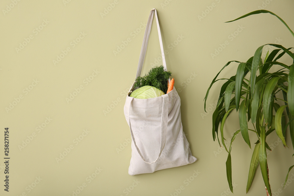 Eco bag with fresh vegetables hanging on wall