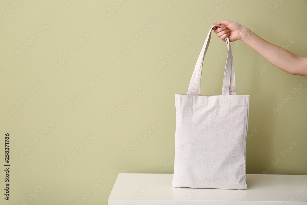 Female hand with eco bag on table against color background