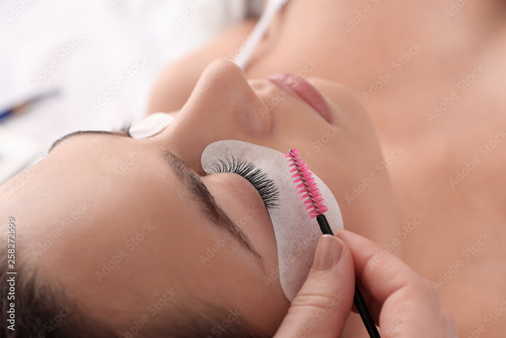 Young woman undergoing eyelash extension procedure in beauty salon, closeup