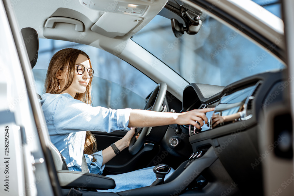 Young woman touching car monitor while sitting in the modern car in the city